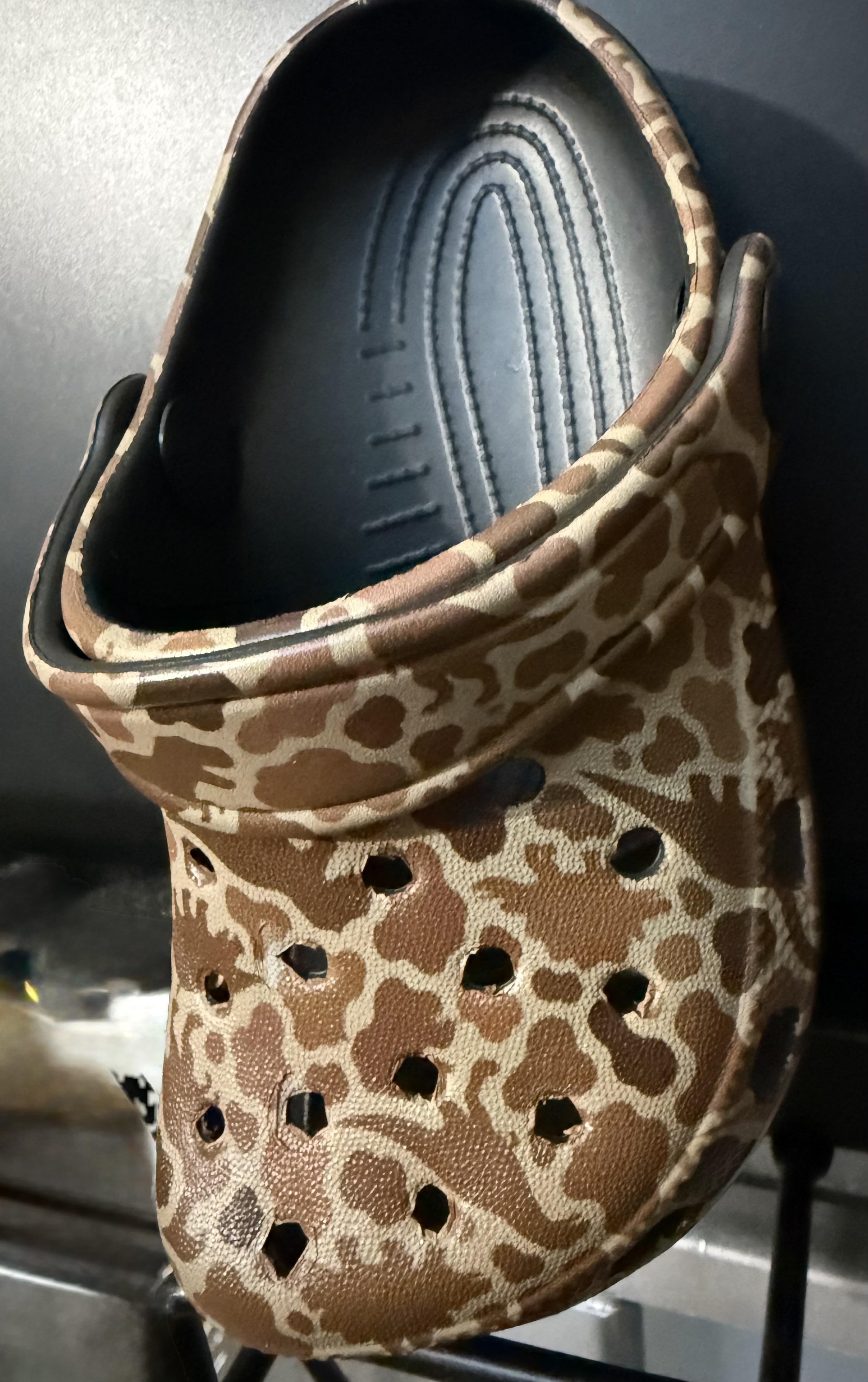 Close-up of one customized Crocs shoe with a brown-and-tan dinosaur pattern across the upper and strap, and a black interior.