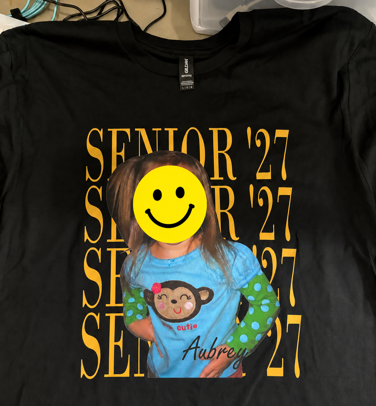 Our personalized black Senior 27 shirt with the printed child's face covered by a yellow smiley.